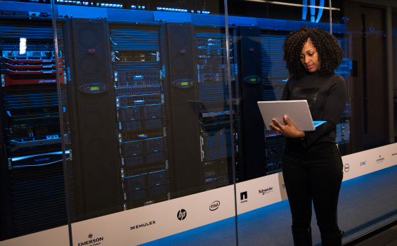 Woman holding a lap top stands in front of servers