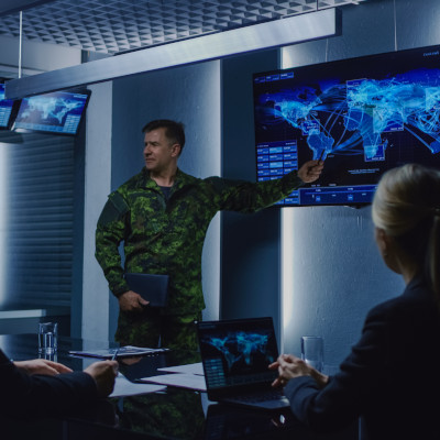 Man in military uniform, pointing to a screen with a map of the world, speaking to an audience