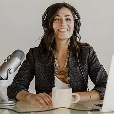 Image of woman smiling with headphones on and a microphone in front of her