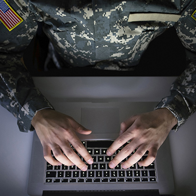 Top view of person in a military uniform, with hands on a laptop, typing